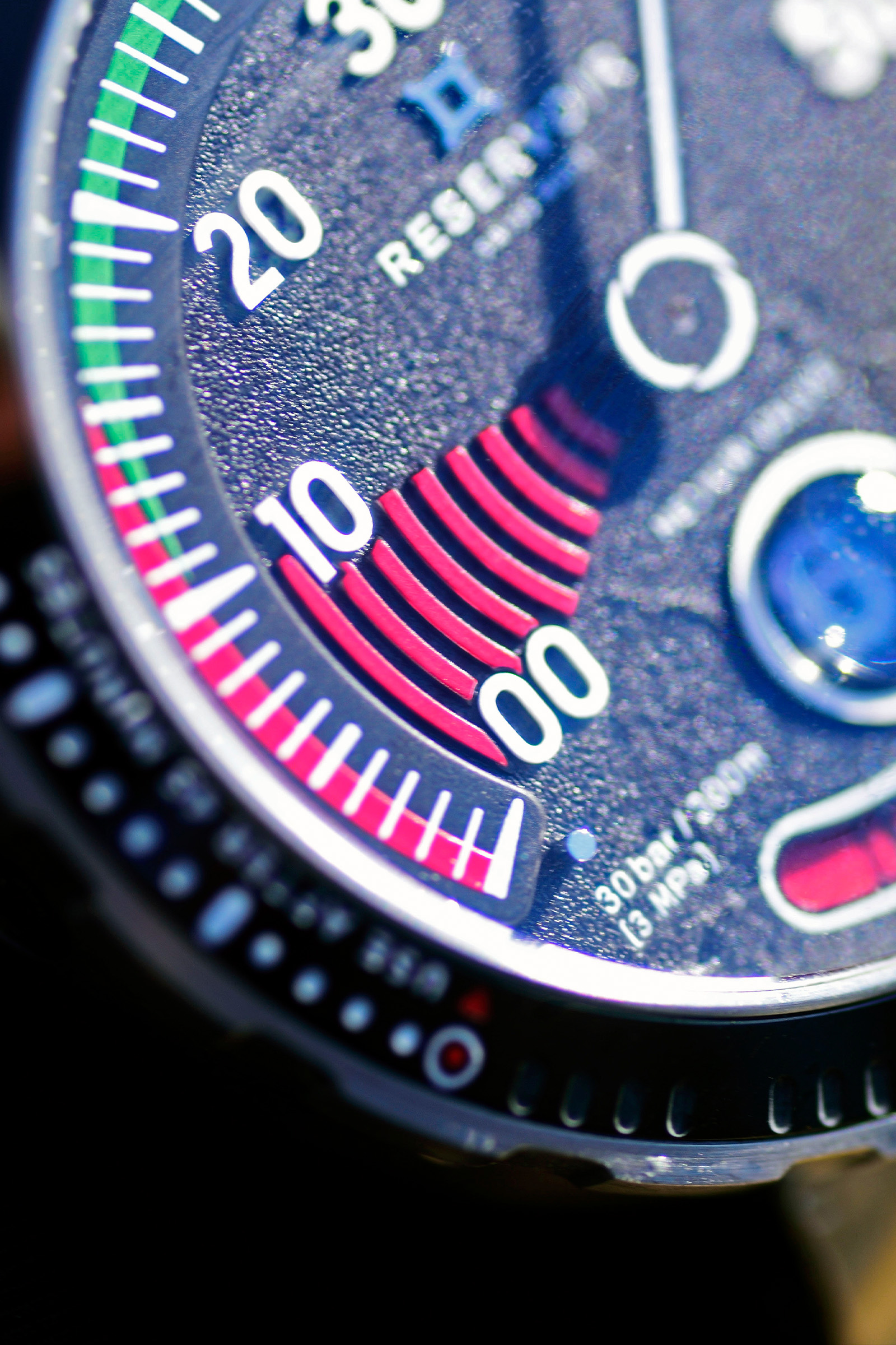 Primer plano de la esfera de un reloj con marcas numéricas, escala rojo-verde y texto "30 bar/300 m (3 MPa)".