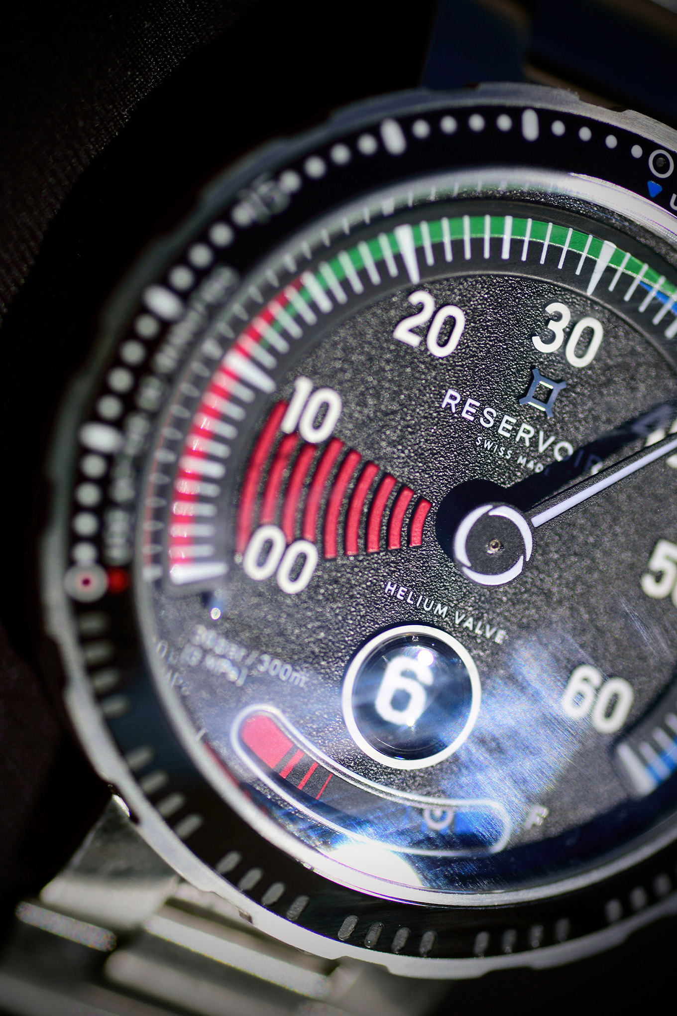 Primer plano de la esfera de un reloj de pulsera que muestra la esfera numerada, los indicadores de color y la "Reservoir Helium Valve".