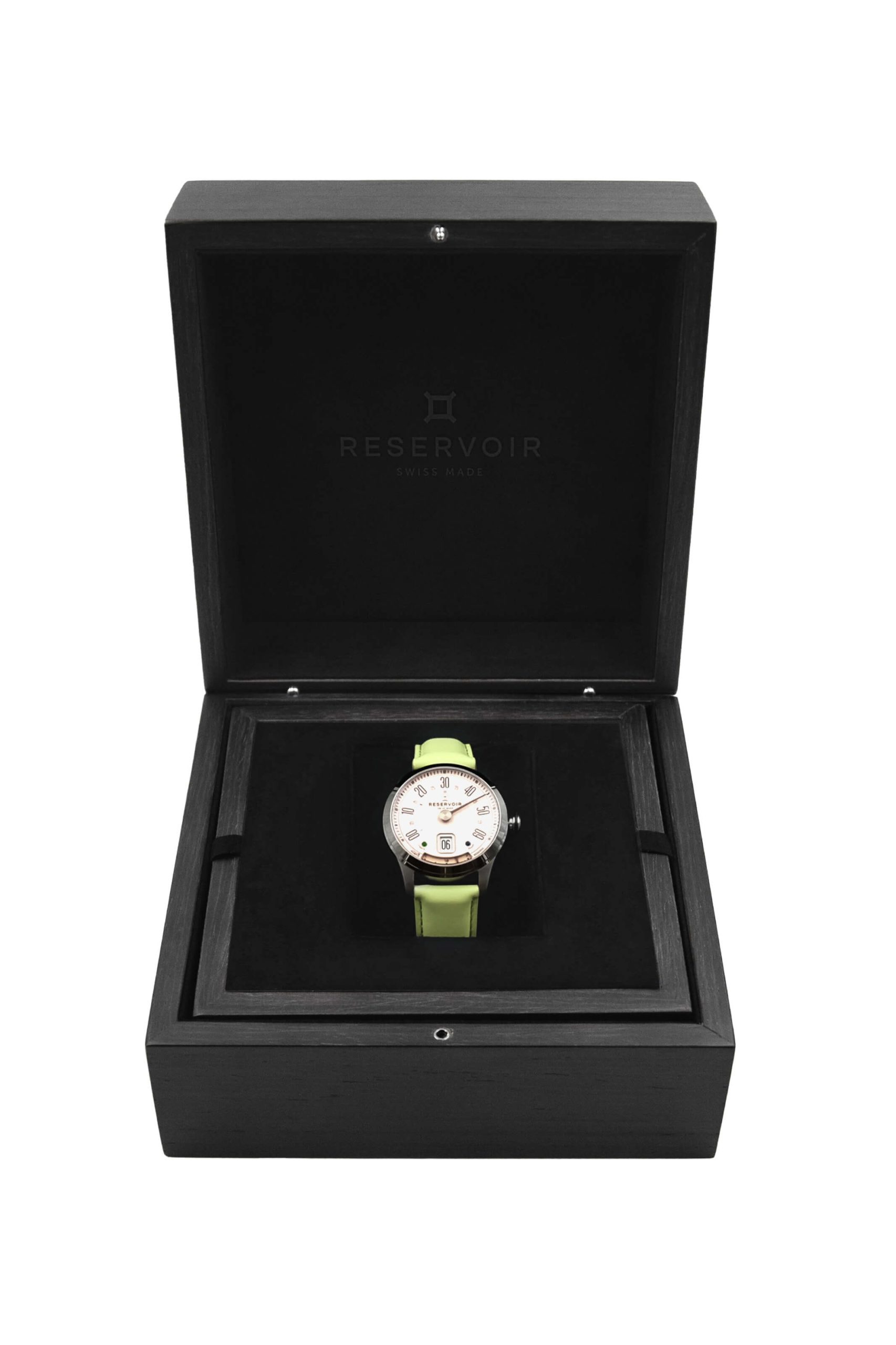 Montre-bracelet avec cadran blanc et bracelet vert clair dans une boîte noire ouverte écrin avec le texte "RESERVOIR SWISS MADE".
