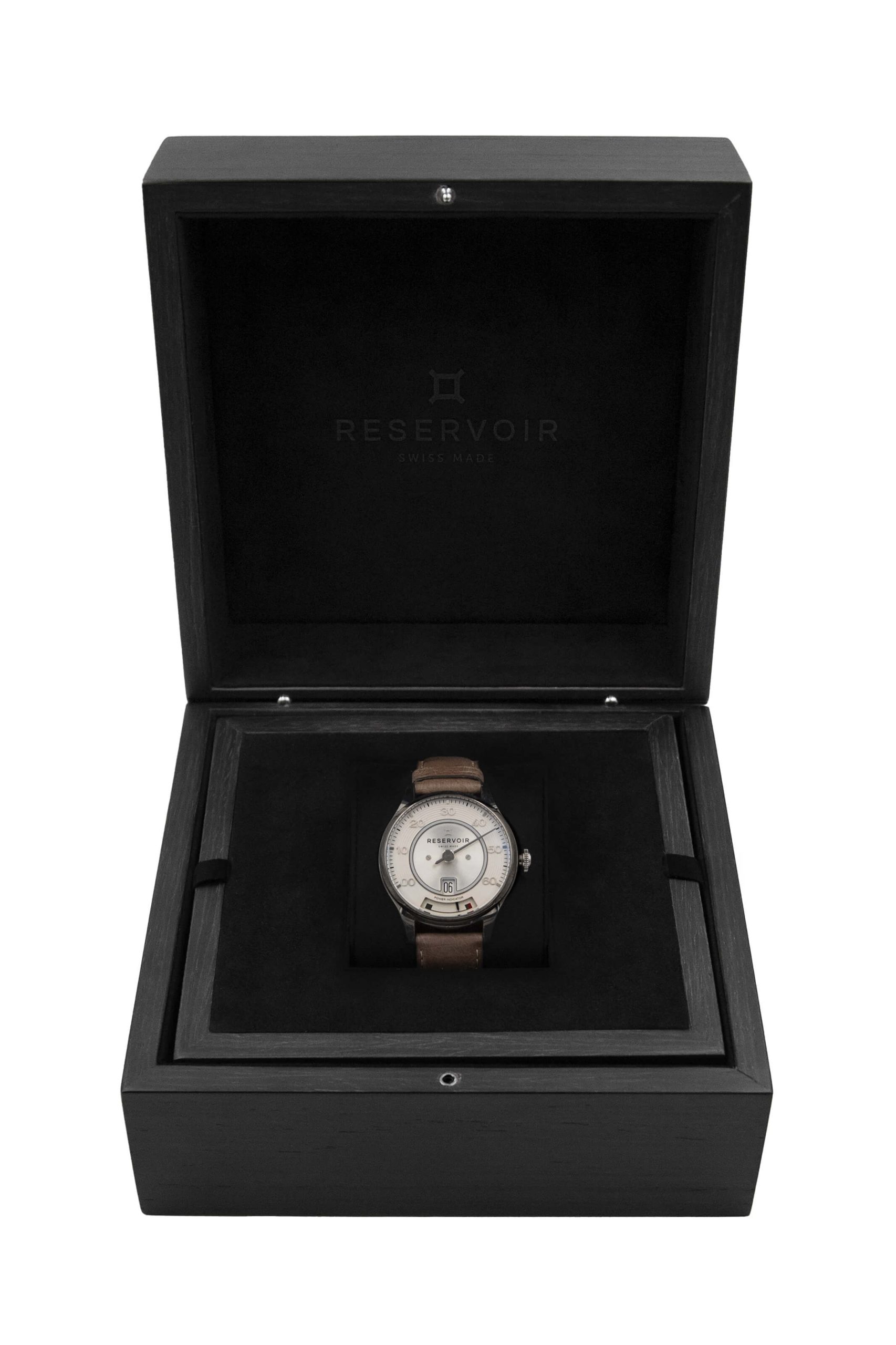 Wristwatch with tan leather strap in black Reservoir box, labeled "Swiss Made" inside lid.