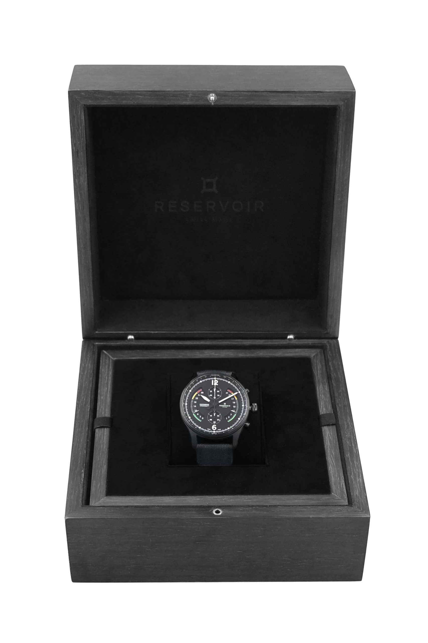 Montre-bracelet noire dans une présentation ouverte écrin avec le nom de la marque "Reservoir" à l'intérieur.
