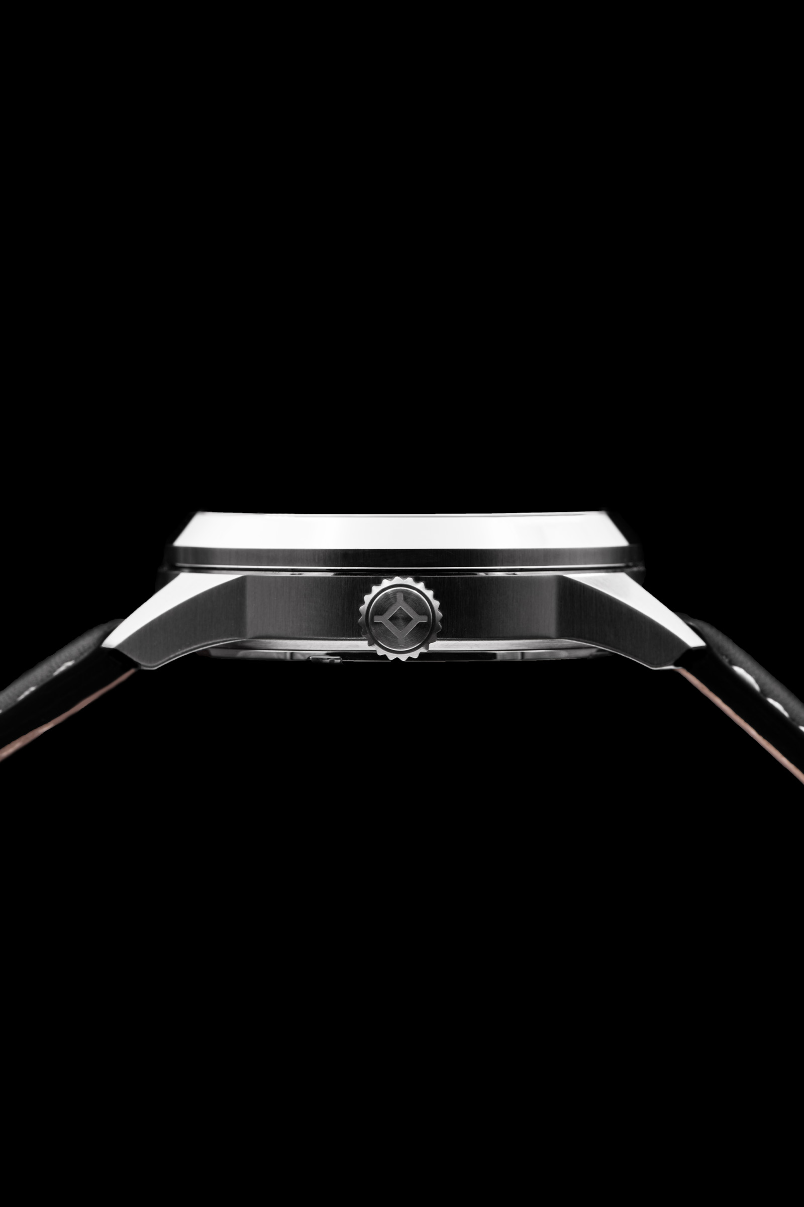 Perfil lateral de reloj de pulsera plateado con logotipo de la corona, bisel plano y correa de piel negra sobre fondo negro.