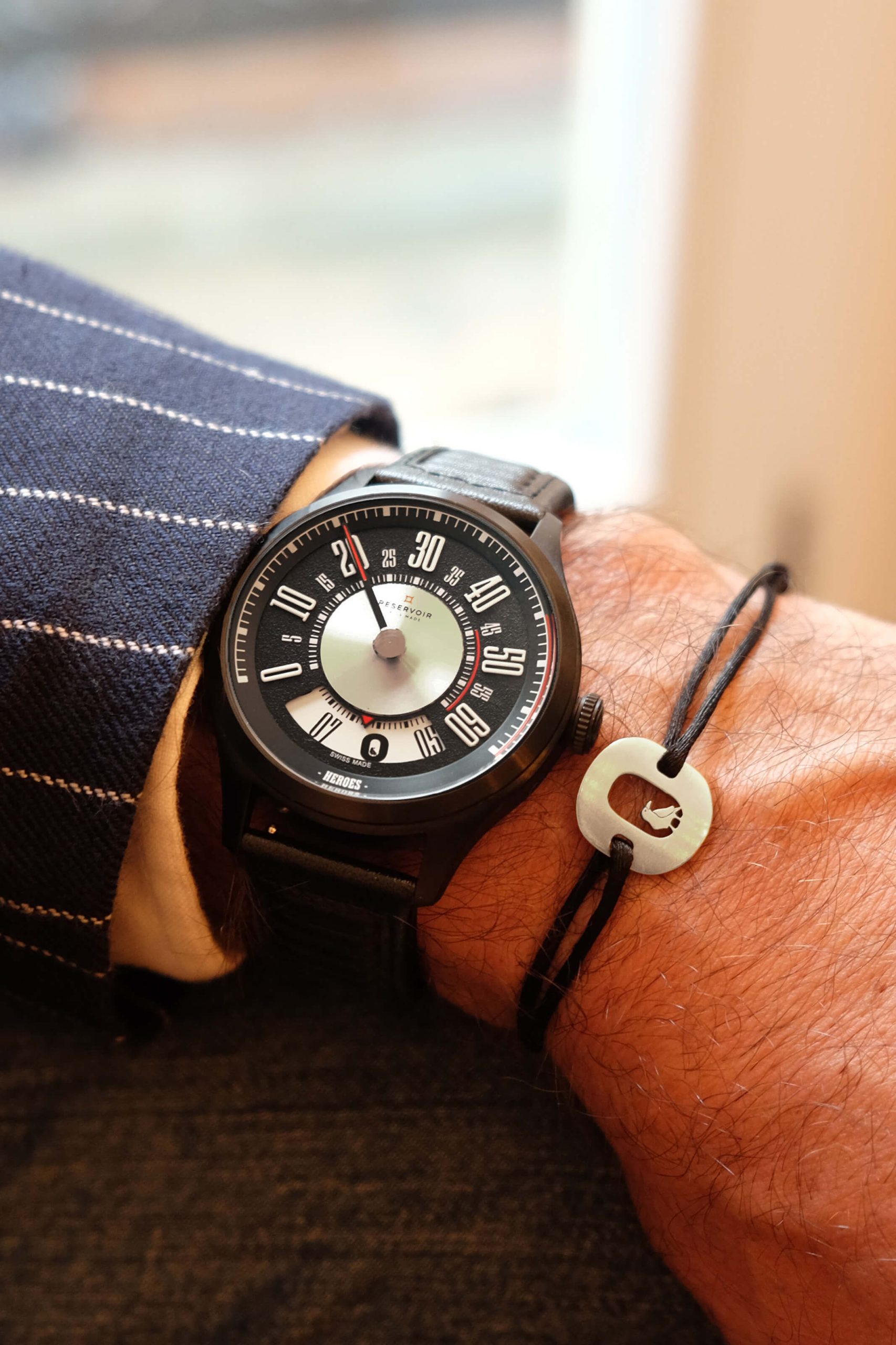 Montre en cuir noirbracelet avec un cadran unique et des chiffres audacieux, portée avec un bracelet et une breloque noirs.