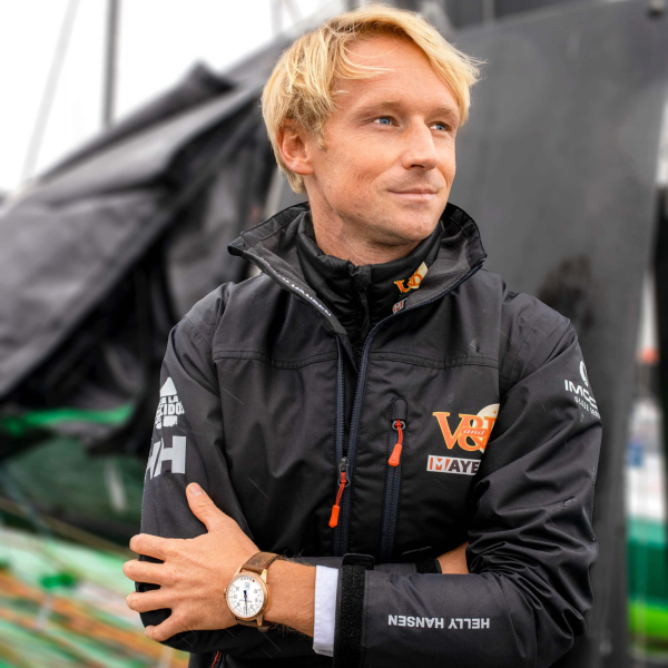 Person with blond hair in a black Helly Hansen jacket with logos and a watch with a brown strap.