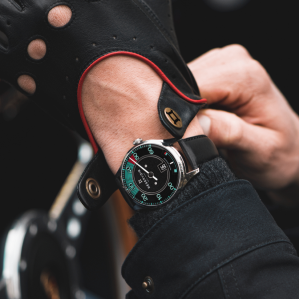 Close-up of gloved hands adjusting a black leather wristwatch with teal and red accents.
