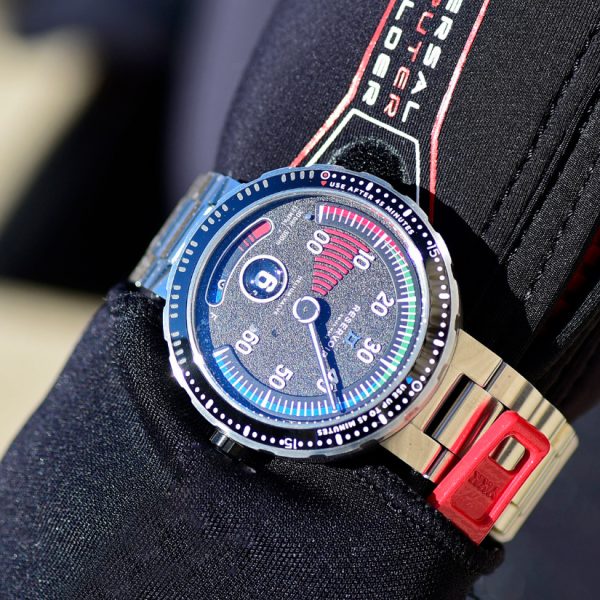 Wristwatch with metal case and bracelet, blue and red detail, unique dial and red clasp over black fabric