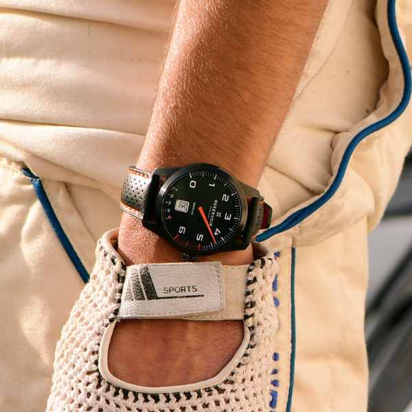 Person in beige racing attire with blue piping showing sports wristwatch with perforated leather strap.