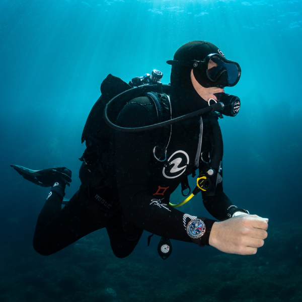 Scuba diver in full gear underwater, surrounded by deep blue water with sunlight streaming down.