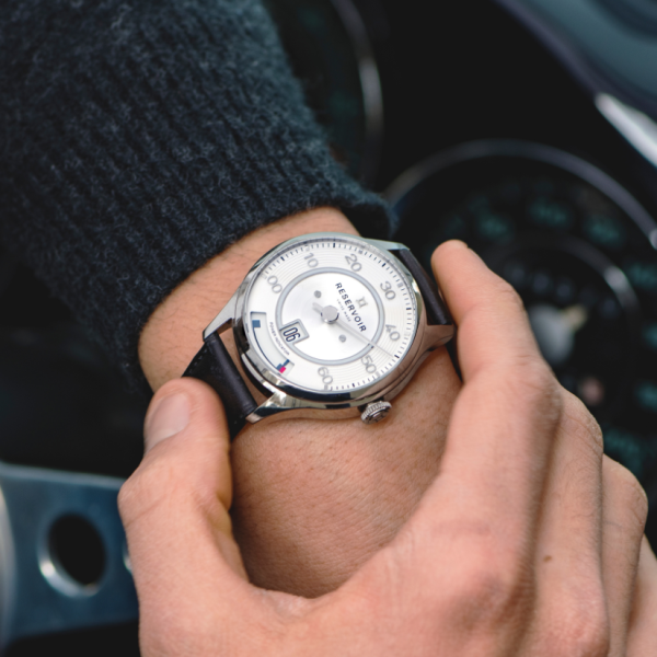 Wristwatch with silver dial, black numerals, and leather strap worn on a wrist, brand "Reservoir".