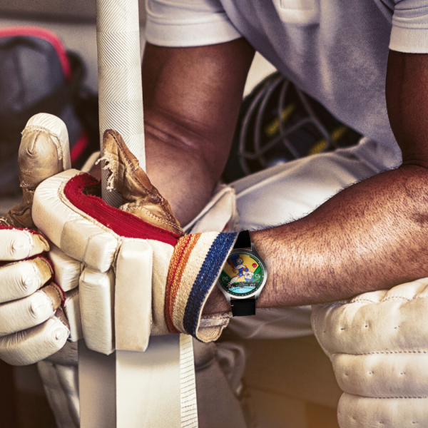 Person in cricket gear with padded gloves, gripping a cricket bat, colorful wristwatch, helmet behind.