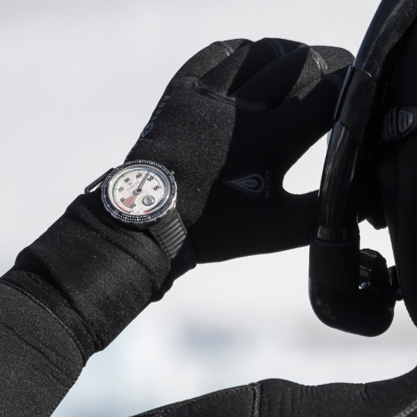 Person in black neoprene gloves holding snorkel, wearing dive watch with multiple dials and markings.