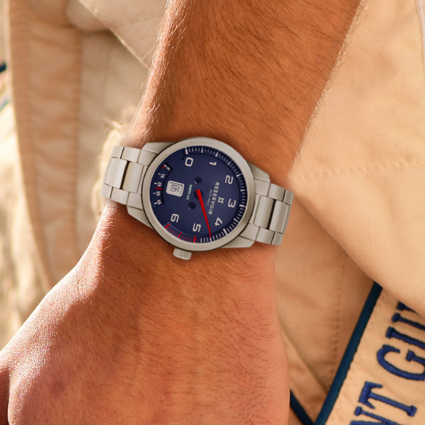 Close-up of a wrist wearing a stainless steel watch with blue dial, white numerals, and a metal link bracelet.