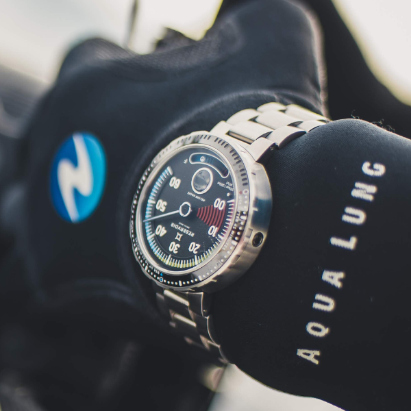 Wristwatch with a metal band and black dial on a black glove marked "AQUA LUNG" and a blue logo.