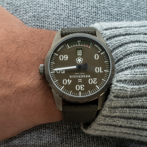 Wristwatch with green dial, white markers, numerals, power reserve, date window, gray knit sweater.