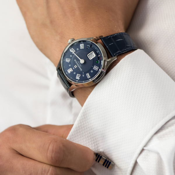 Person adjusting white dress shirt cuff with a blue wristwatch and striped cufflink.