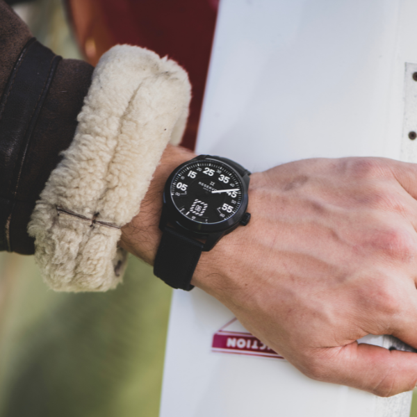 Person wearing a black wristwatch with white numbers, furry cuff jacket, holding a white object.