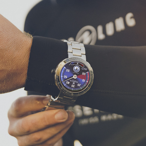 A person in a black wetsuit wearing a metallic wristwatch with numerical readings on the round dial.