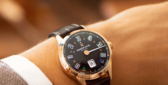 Une montre-bracelet avec cadran noir, chiffres blancs et affichage de la date sur un poignet, portant un blazer à carreaux.