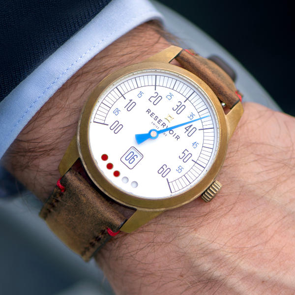 Close-up of a wristwatch with brass case, white dial, brown leather strap, and blue hand indicating time.