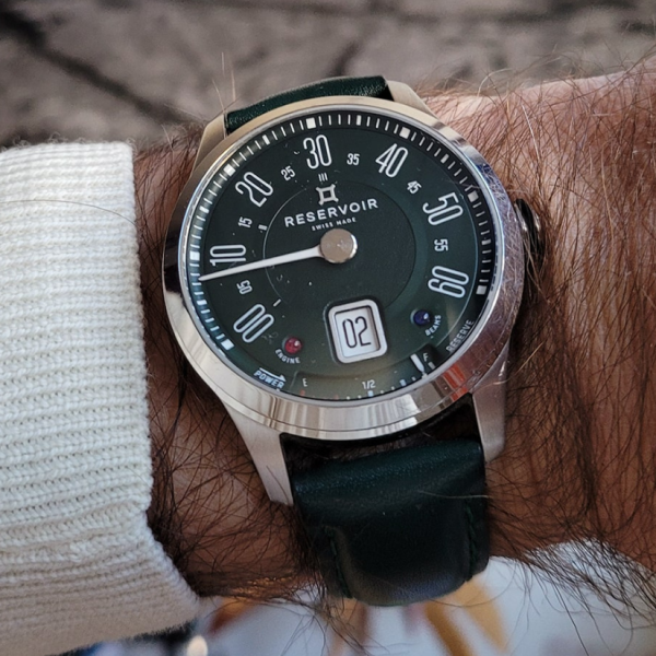 Dark green dial and strap wristwatch with large white numerals worn on an arm, shows brand name RESERVOIR.