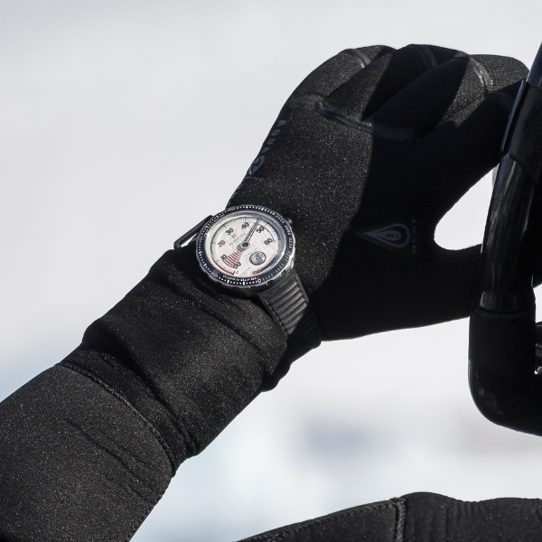 Person in black gloves adjusting a black wristwatch with a white dial and visible markings.