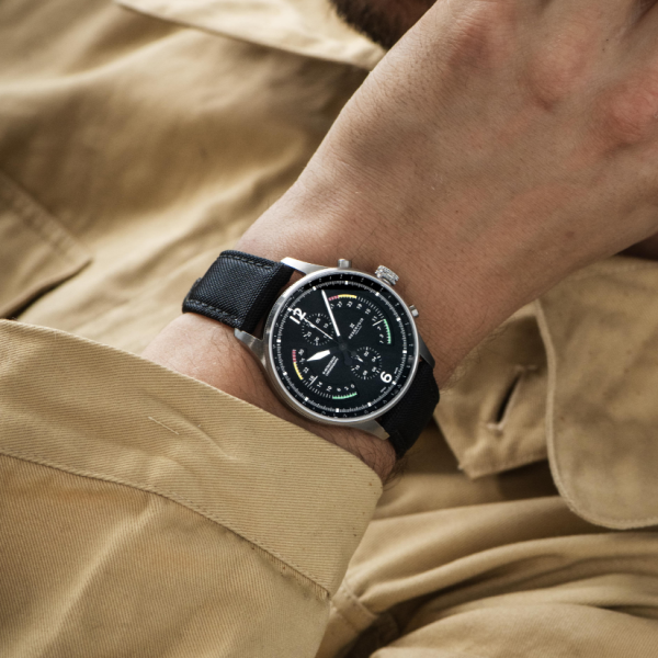 Person in beige shirt showing wristwatch with black strap, round black dial, and silver case.