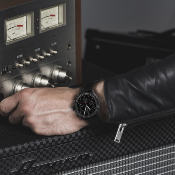 Adjusting knobs on a vintage amplifier, person in black leather jacket and wristwatch with black strap.
