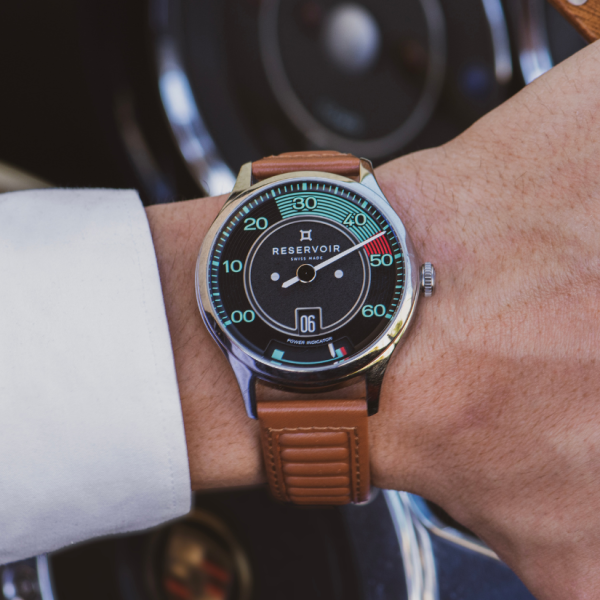 Wristwatch with black dial, brown leather strap, "RESERVOIR SWISS MADE" text, numeric scale on wrist.