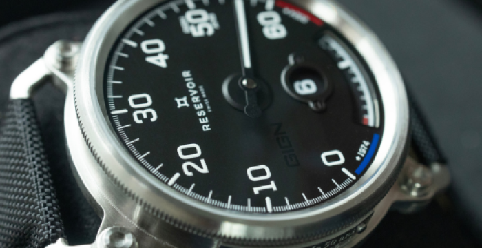 Close-up of a black-dial wristwatch with large numerals, power reserve indicator, and black strap.
