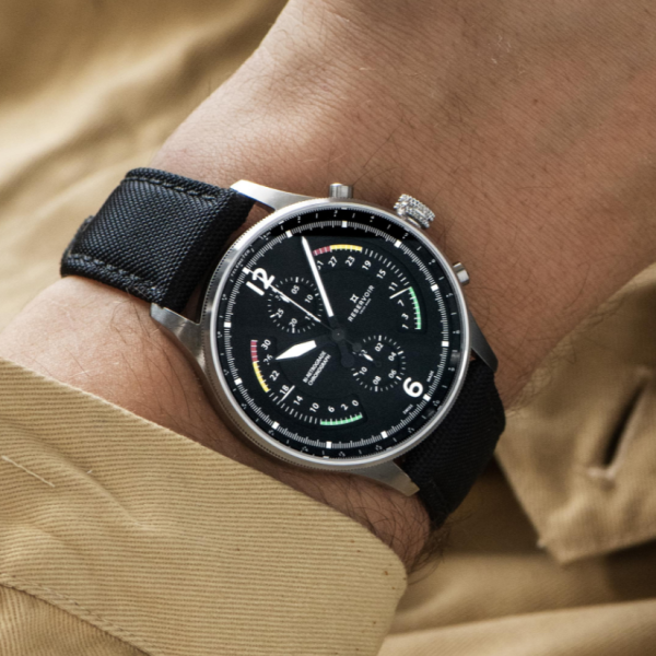 Wristwatch with black dial, subdials, colorful indicators, silver frame, black strap, beige sleeve.