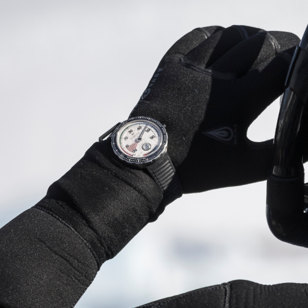 Person in black gloves holding bicycle handlebar with sports watch on left wrist, outdoor background.