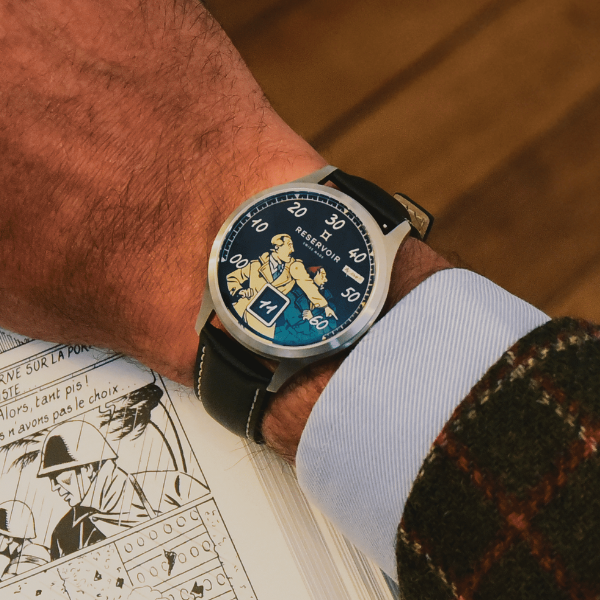 Wristwatch with cartoon dial, black strap, retrograde minute and date, over comic book page.