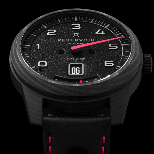 Close-up of a Reservoir wristwatch with black dial, large white numerals, red hand, and black strap.