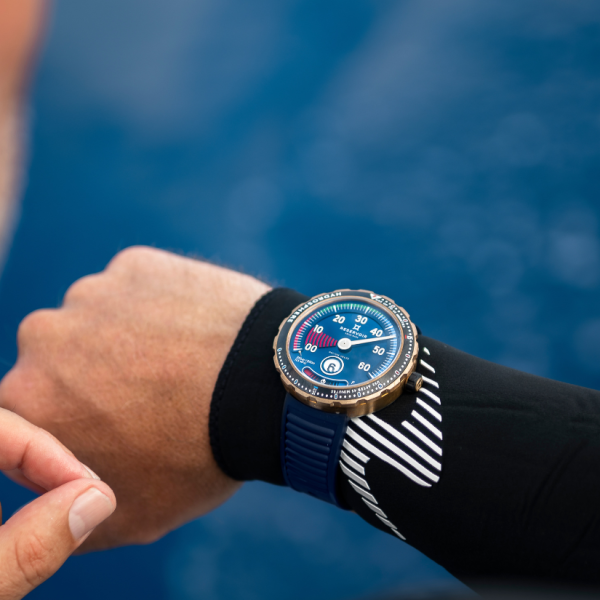 Wrist wearing diver's watch with blue dial, red and white markings, blue strap, in aquatic setting.