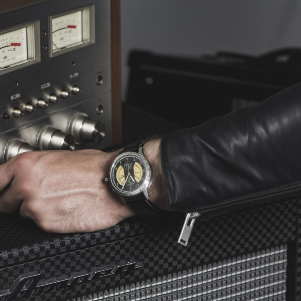 Hand wearing a black strap watch adjusting knobs on vintage amplifier with analog meters.