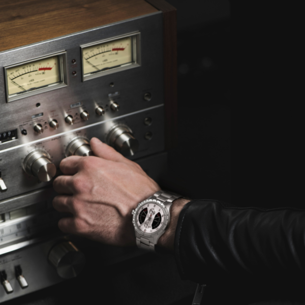 Hand with silver wristwatch adjusting knobs on vintage audio equipment with analog meters.