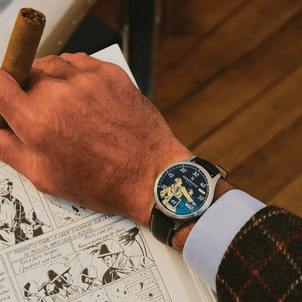 A person holds a cigar and reads a French comic, wearing a blue watch, shirt, and checked blazer.