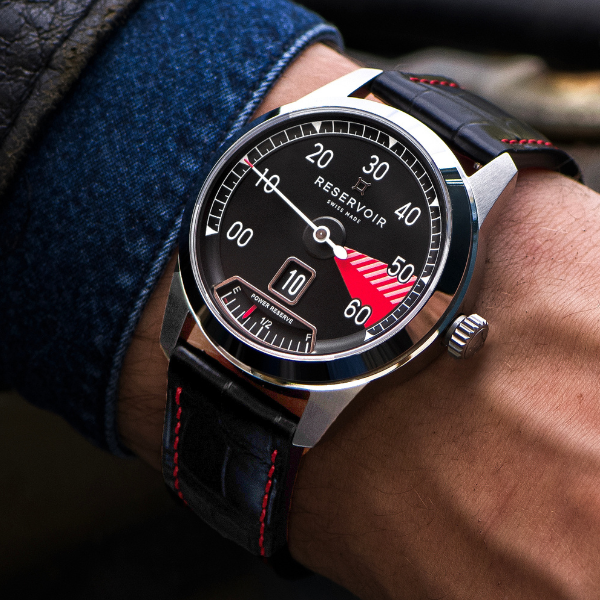 Wristwatch with black dial, meter-like design, stainless steel case, black leather strap, worn on wrist.
