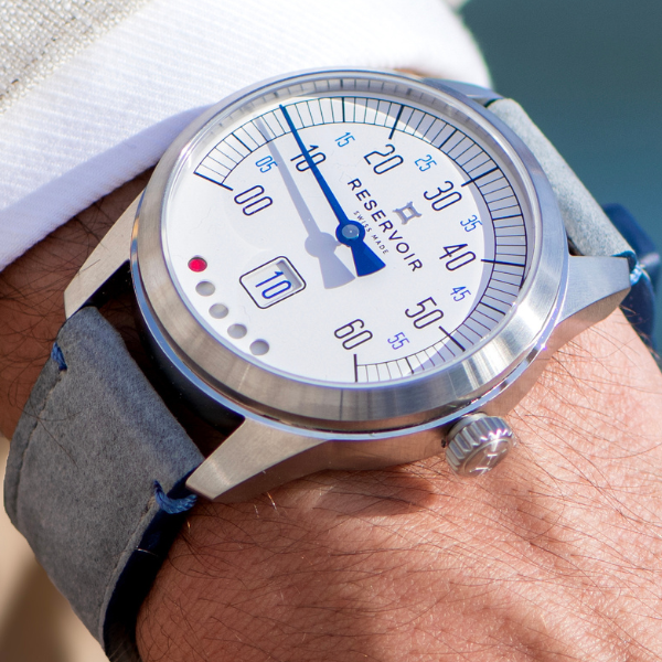 Wristwatch with speedometer-like dial, blue hand, silver case, grey strap, and “Reservoir” brand name.