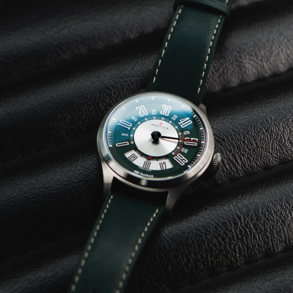 Wristwatch with dark green strap, silver case, mix of numerals on dial, on textured black surface.