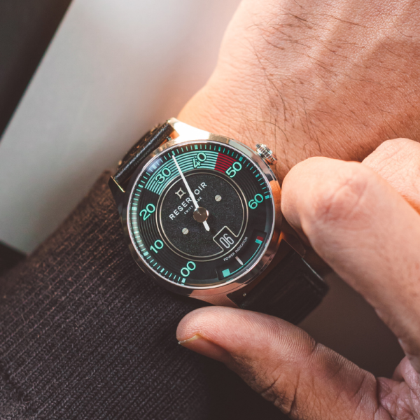 Person adjusting wristwatch with black dial, green and red indicators, date at 6 o'clock, black strap.