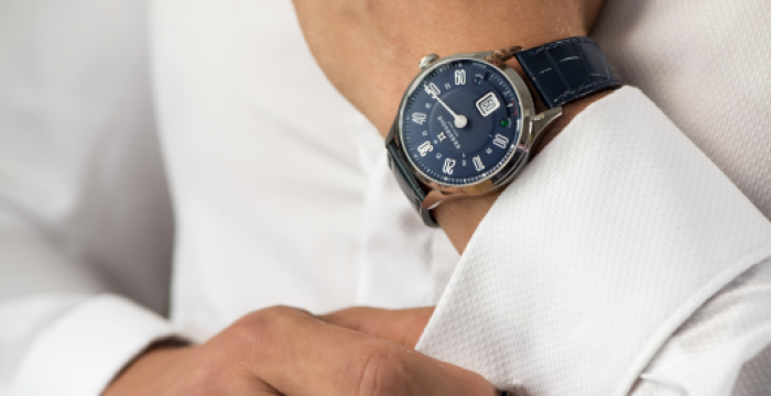 Person adjusting white dress shirt cuff, wearing blue-dial watch with blue leather strap and date display.