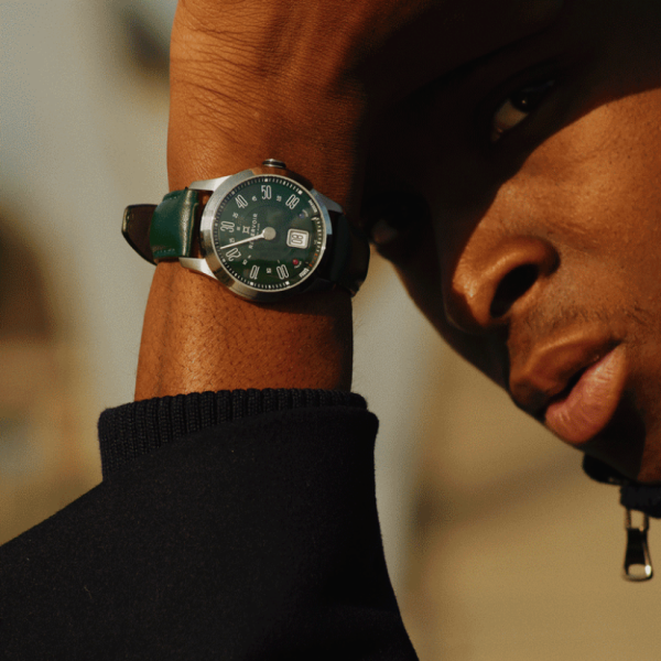 Person with arm raised, wearing a dark sleeve and green watch, blurred background.