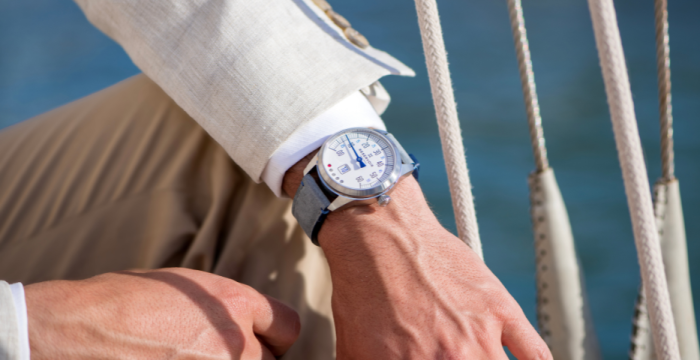 Person in beige blazer, khaki pants, wearing wristwatch near taut ropes in nautical setting.