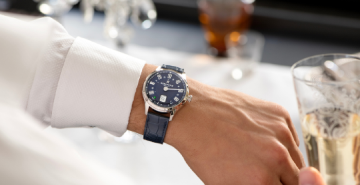 Person in a white shirt wearing a blue wristwatch holds a glass with a light-colored drink.