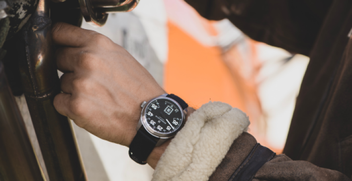 Person wearing a shearling-lined brown jacket and digital watch, gripping metallic equipment.