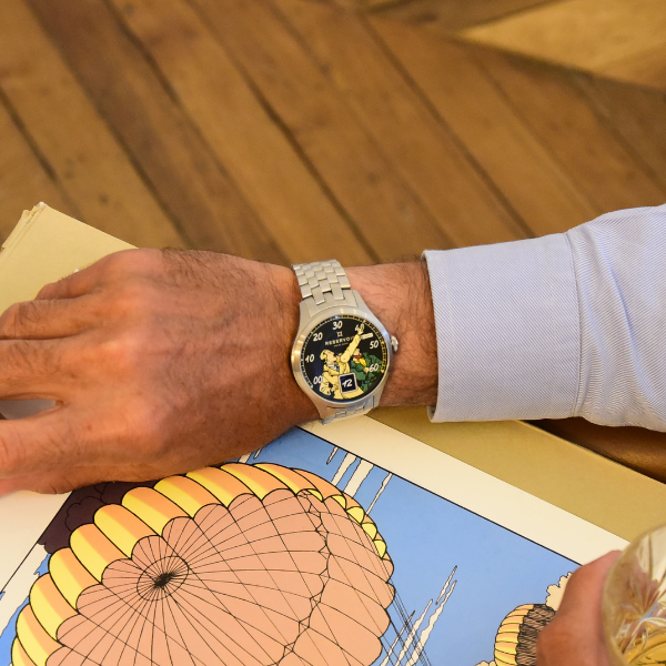 Person wearing silver watch, light blue shirt, browsing illustrated book on wooden floor.