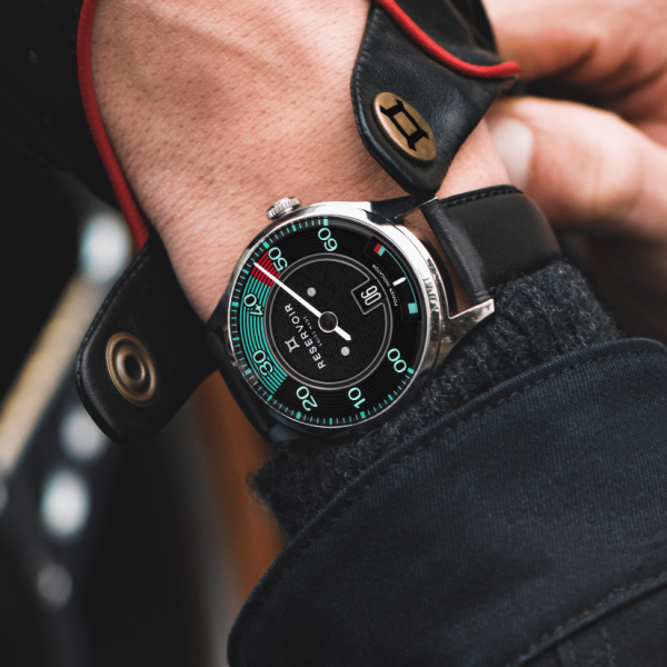 A person wearing a Reservoir watch with an automotive-style dial, and a black leather jacket.