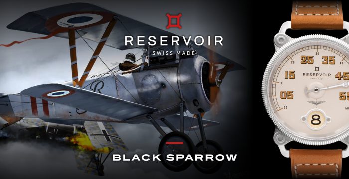 WW1 pilot wearing a leather jacket and flying a biplane, holding a light greyish beige watch against a dark black and medium greyish blue sky.