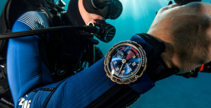 Scuba diver underwater wearing a detailed blue and gold wristwatch on their left wrist.